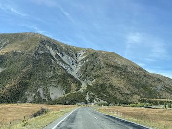 Country road by mountains against sky