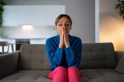 Sad woman in blue sweater sits on comfortable sofa and suffers from autumn depression at home