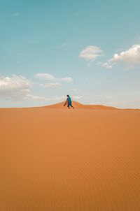 Man on sand dune in desert against sky