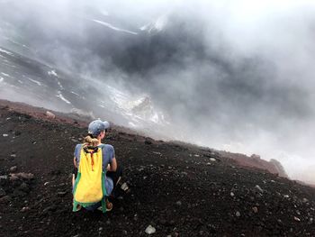 Rear view of mature woman crouching on mountain during foggy weather
