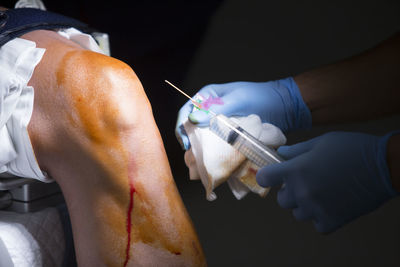 Cropped hands of doctor holding syringe by patient knee in operating room