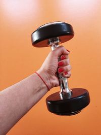 Close-up of woman holding dumbbell against orange background