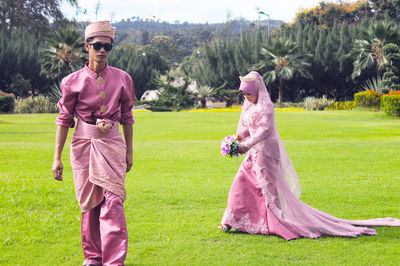 Confident bride and groom in traditional clothing walking on grassy field