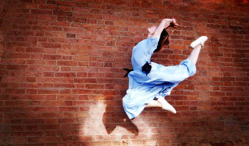 Woman jumping against brick wall