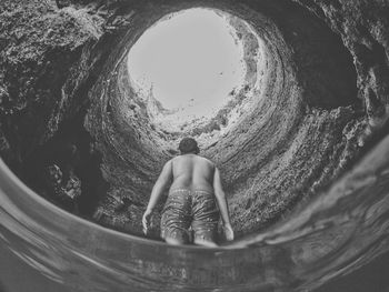 Rear view of shirtless man sitting in tunnel