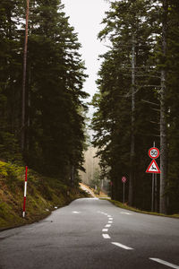 Road sign by trees against sky