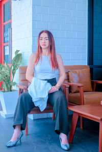 Portrait of woman sitting on chair against wall