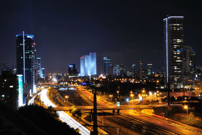 Illuminated street amidst buildings against sky at night