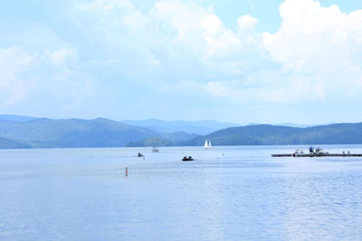 Boats sailing on river with mountains in background against cloudy sky