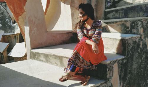 Portraits-young woman looking away while sitting on staircase in sun