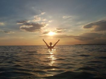 Silhouette person in sea against sky during sunset