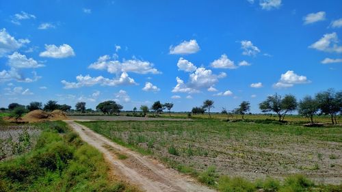 Dirt road amidst field against sky