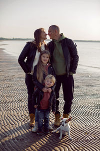 Family in a leather jacket walks along the beach with their dog in autumn