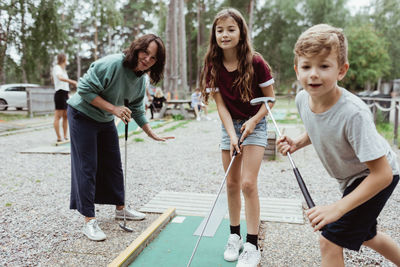 Sibling playing miniature golf with family in backyard during vacation