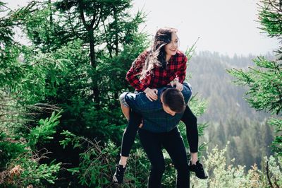 Boyfriend piggybacking smiling girlfriend in forest