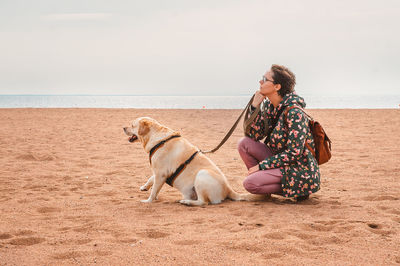 Woman with dog on beach by sea against clear sky