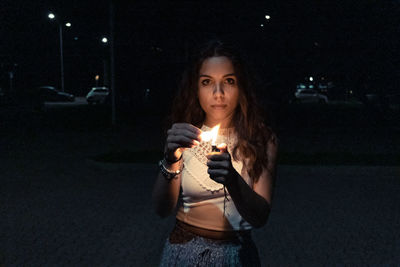 Portrait of young woman standing against illuminated wall