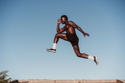 Young male athlete jumping over steps by clear sky during sunset