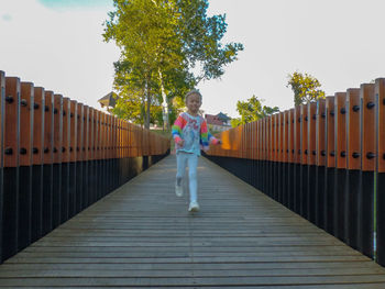 Girl standing on footbridge against sky