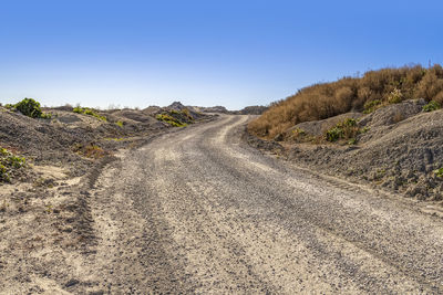 Dirt road amidst land against clear sky