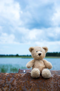 Stuffed toy on rusty metal by lake against cloudy sky