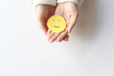 Cropped hand of woman holding orange fruit against white background