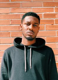 Portrait of young man standing against brick wall