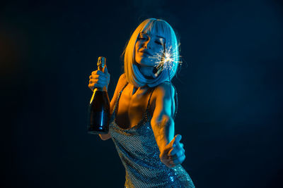Woman in dress with sparkler and champagne standing against black background