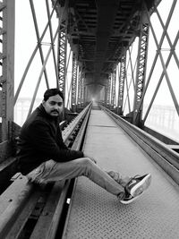 Side view of young man sitting on bridge