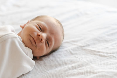 Cute newborn baby boy lying on bed at home looking at  camera