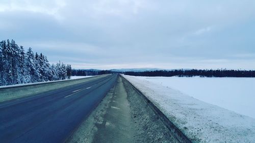 Road by snow covered landscape against sky