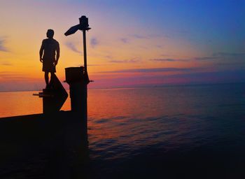 Silhouette man standing on pier over sea against sky during sunset
