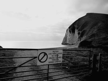 Close-up of information sign on cliff by sea against sky