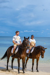 Woman and man riding horse on beach against sky