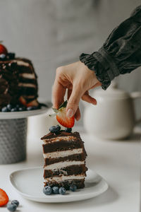 Hand putting strawberry on a chocolate cake