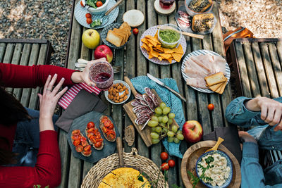 High angle of unrecognizable female friends sitting at wooden table in woods and eating tasty food during picnic in valle del jerte in summer