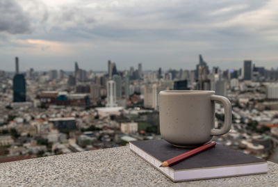 Close-up of coffee cup against buildings in city