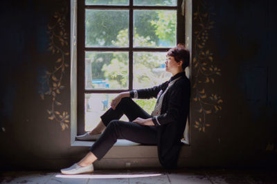 Side view of teenage girl sitting on window sill