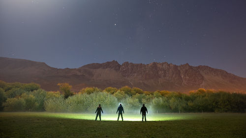 People standing on field against mountain range at night