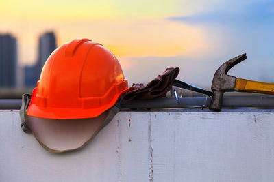 Close-up of red hardhat by hammer and eyeglasses on wall