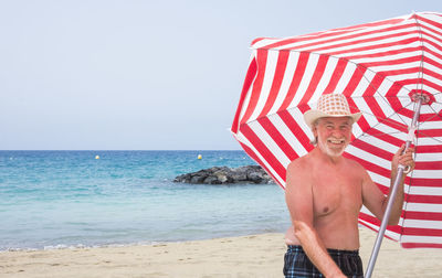 Full length of shirtless man wearing hat at beach against sky