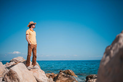 Rear view of man standing at beach against clear blue sky