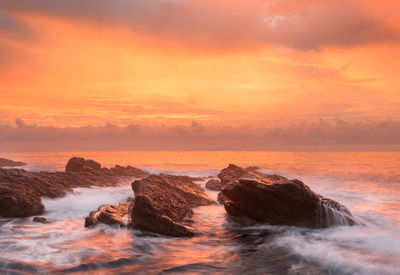 Rocks in sea against romantic sky at sunset