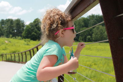 Side view of girl holding packet while looking through railing