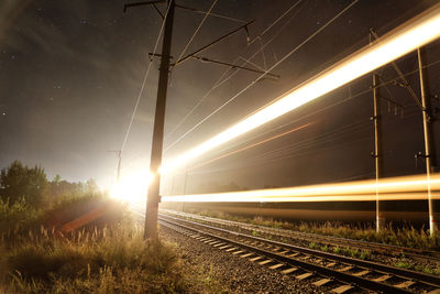 Illuminated railroad tracks against sky at night