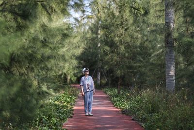 Full length of woman standing on footpath amidst trees in forest