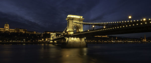 Illuminated bridge over river against sky in city at night