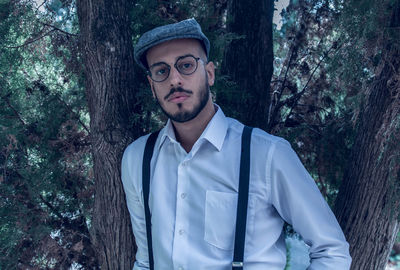 Portrait of young man standing against trees in forest