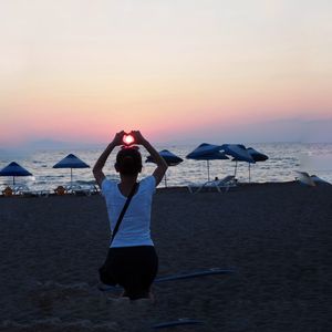 Rear view of woman on beach against sky during sunset