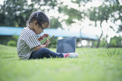 Young woman using laptop while sitting on field